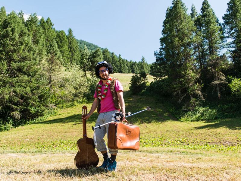 Foto di un volontario che si vede nella natura con valigia, chitarra e il necessario per andare in una colonia estiva o in un campo estivo